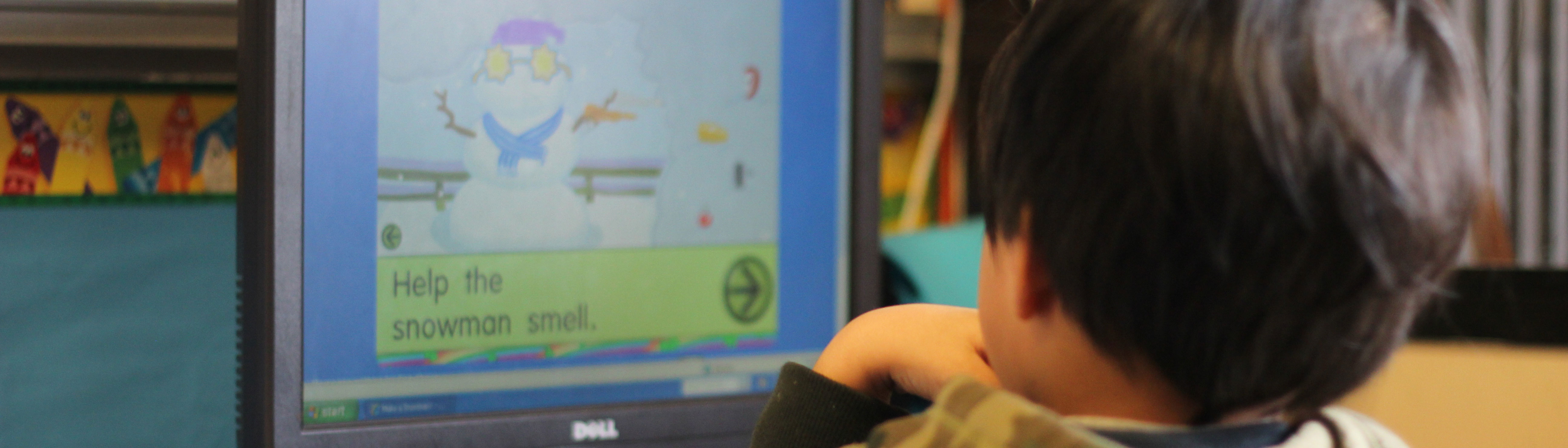 Preschooler playing on a desktop computer in a childcare setting.